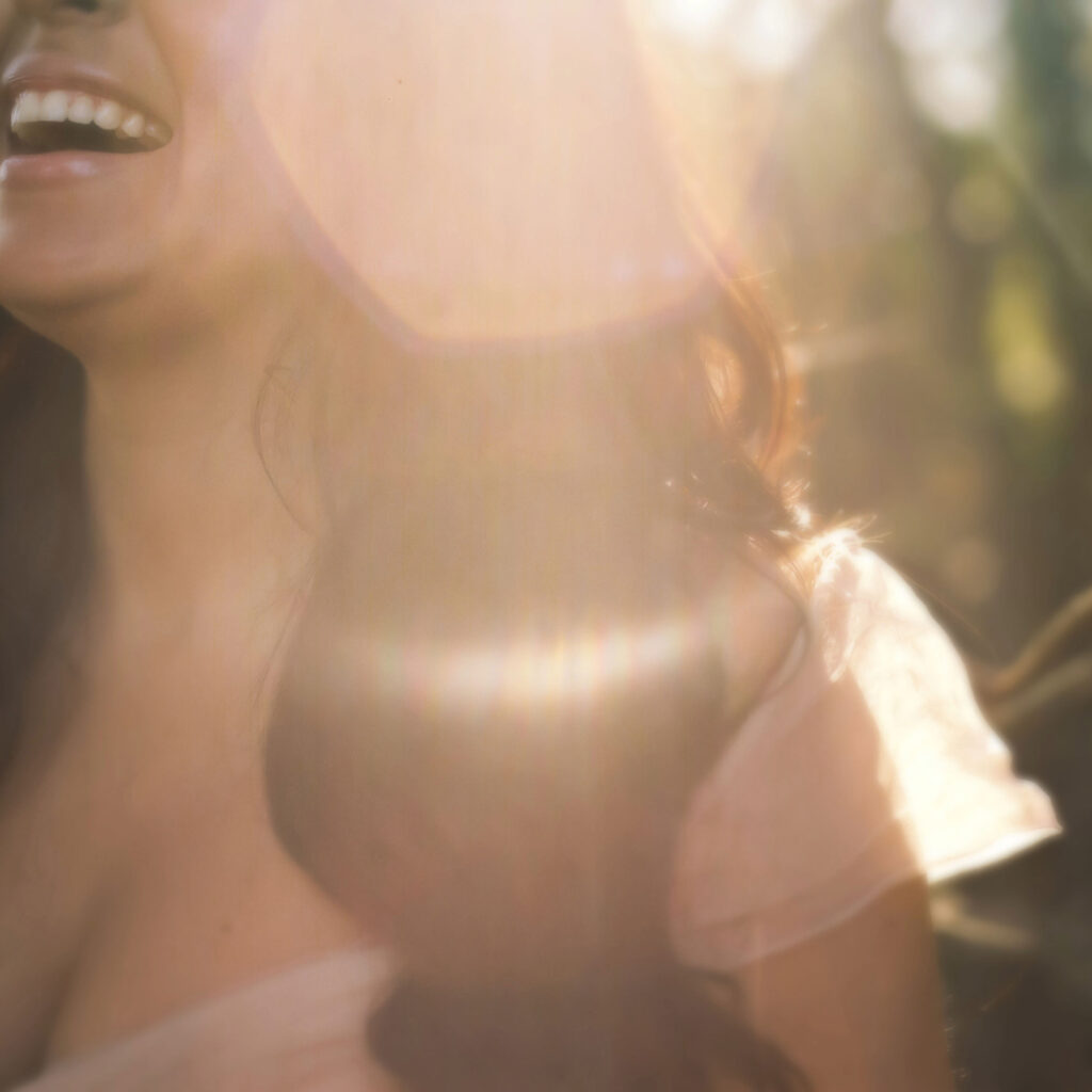 a woman is smiling in the sun to illustrate the Benefits from Acts of Kindness